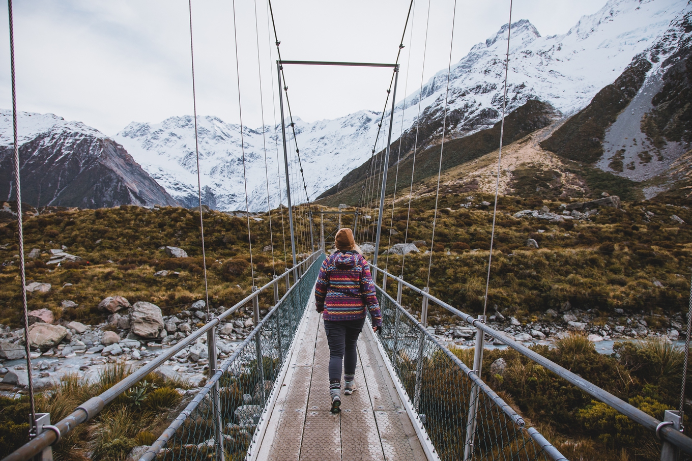Amanda enjoys one of the many walks near Aoraki Mount Cook A woman on a hike; she is on a bridge with a mountain in the background