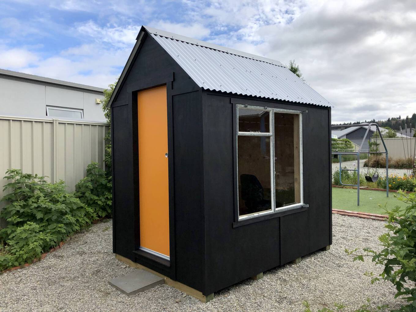 The finished product! A photo of the finished Writer's Studio - it has a corrugated iron roof, orange door and is painted black with a big window on the side